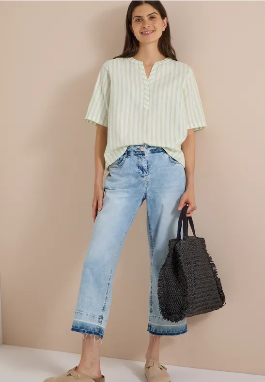 Femme en chemise rayée vert-blanc, jeans larges et sac noir tressé.