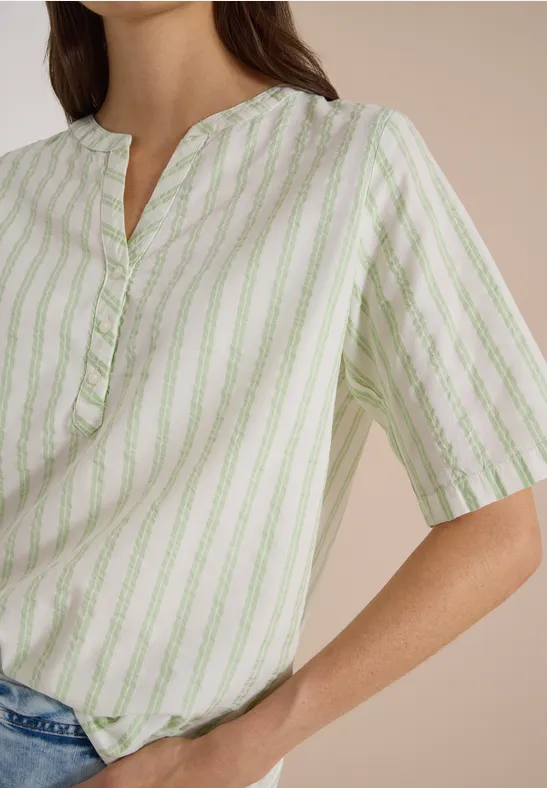 Femme en chemisier ample rayé blanc et vert clair à manches courtes, élégamment rentré dans un jean.
