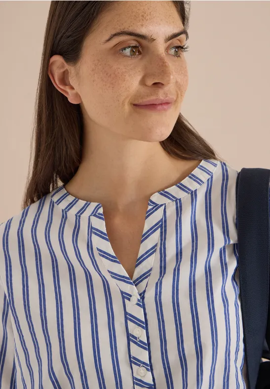 Femme aux cheveux bruns porte un chemisier blanc à fines rayures bleues et col en V.