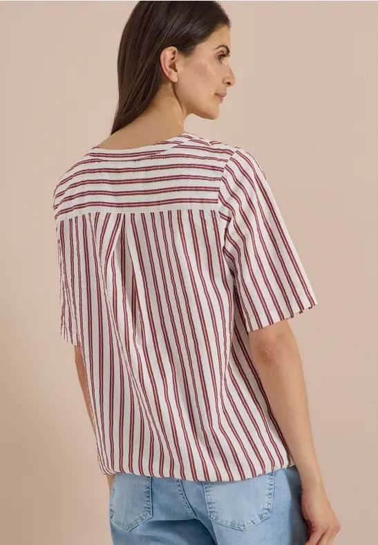 Femme vue de dos portant un top à rayures et un jean sur fond neutre.