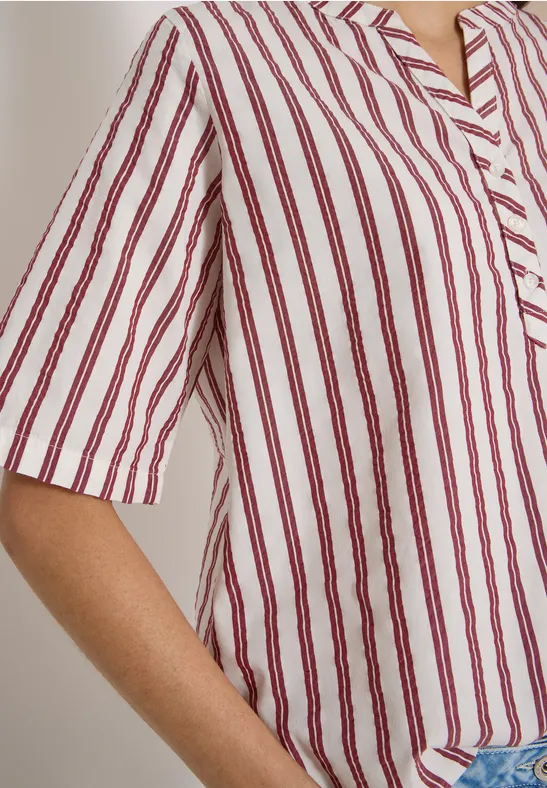 Épaule et bras vêtus d’une chemise blanche à fines rayures rouges, coupe décontractée.
