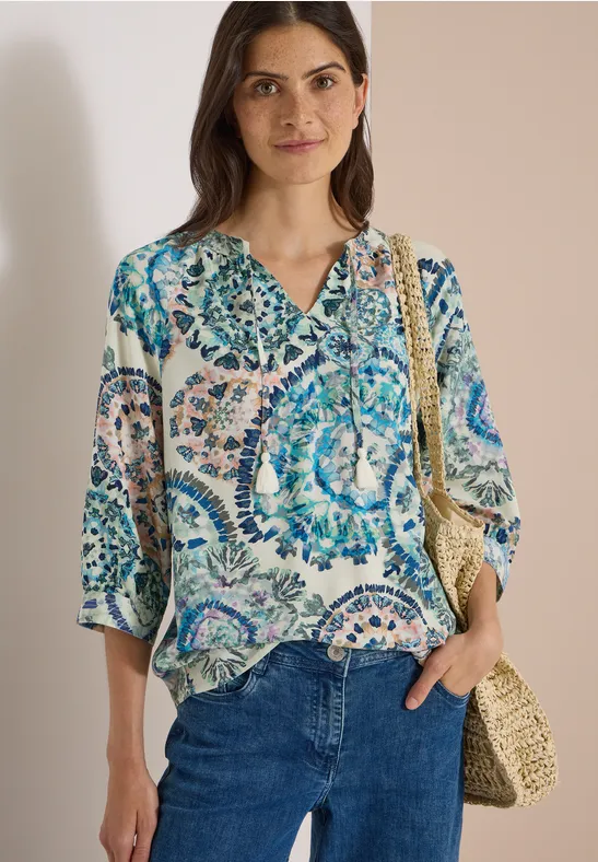 Femme portant un chemisier à motifs bleus et verts, jean et sac en osier