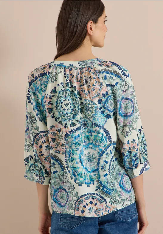 Femme de dos portant un chemisier à imprimé mandala bleu et beige.