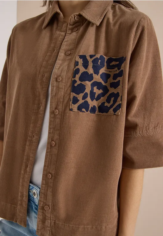 Braunes Hemd mit kurzen Ärmeln und auffälliger dunkelblauer Leoprint-Tasche auf der Brust.