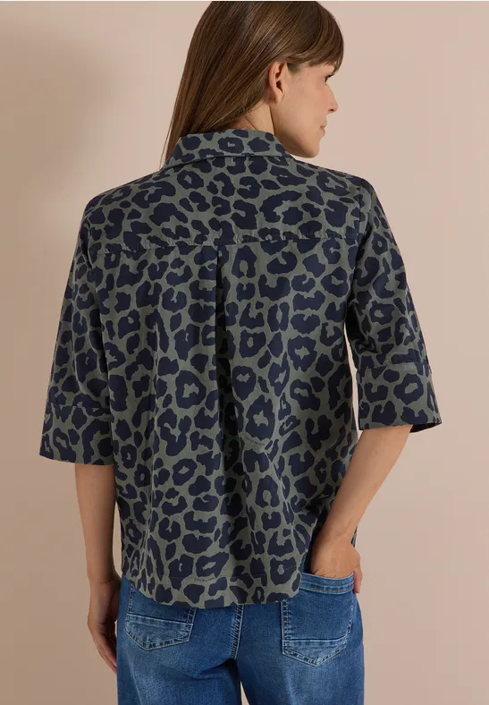 Rückansicht einer Frau in lockerer Leopardenprint-Bluse mit halben Ärmeln und Jeans, Hand in Hosentasche.