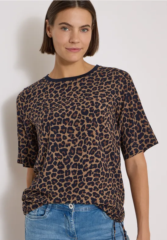 Frau in lässigem Leo-T-Shirt und Jeans vor hellem Hintergrund.