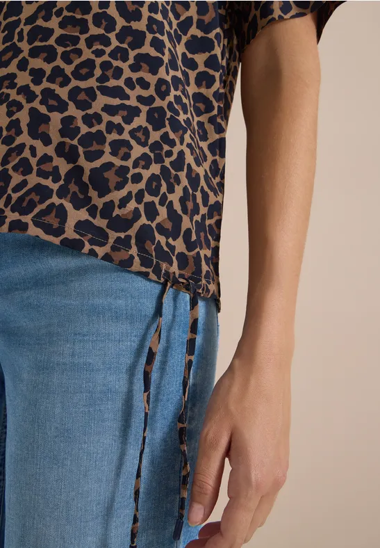 Nahaufnahme eines Unterkörpers in blauer Jeans und Leopardenmuster-Bluse mit seitlichen Schnürungen