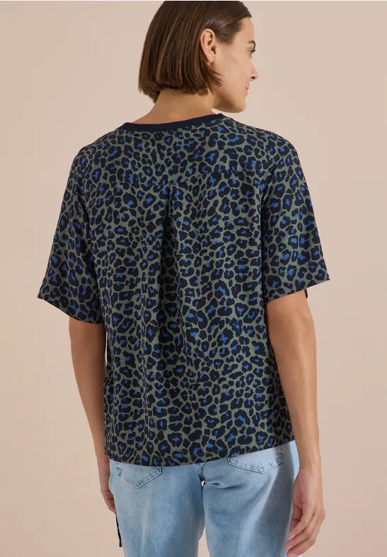 Frau von hinten in lockerem, kurzärmeligem Shirt mit blau-schwarzem Animal-Print und Jeans.