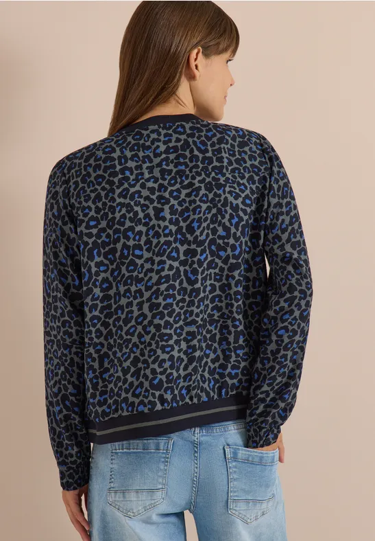 Femme vue de dos portant un pull léopard bleu et noir avec un jean bleu clair.
