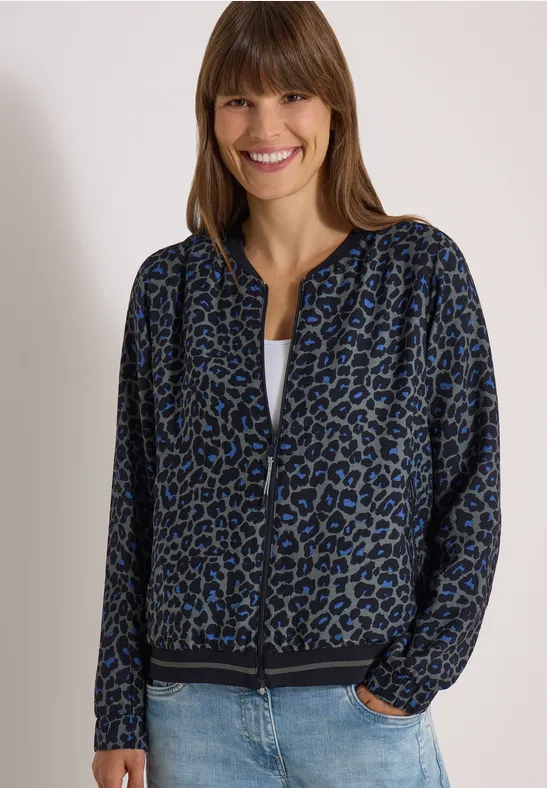 Femme souriante en veste léopard bleue, tee-shirt blanc et jean.