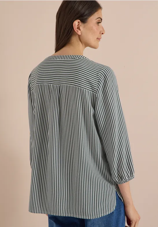 Rückenansicht einer Frau in lockerer, schwarz-weiß gestreifter Bluse mit 3/4-Ärmeln vor beigem Hintergrund