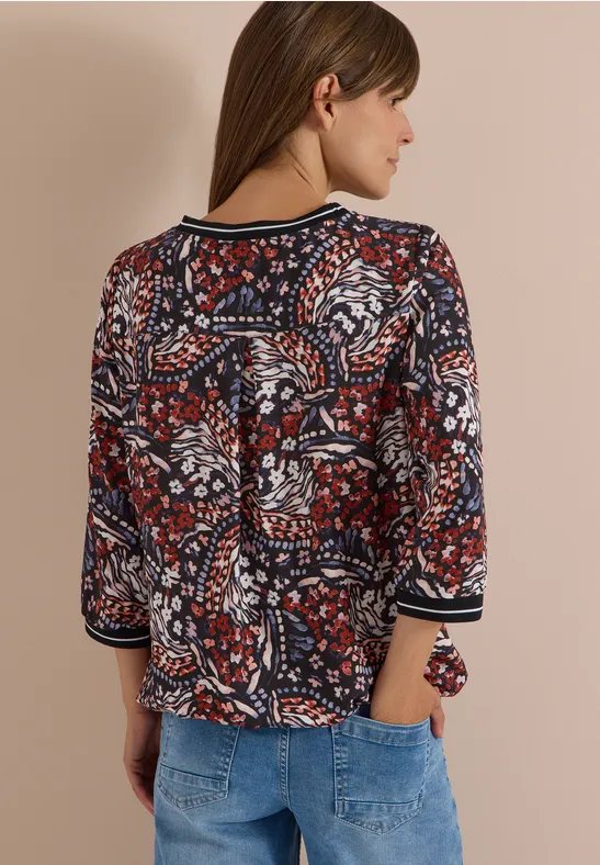 Femme de dos portant un chemisier à motifs rouge et bleu à manches trois-quarts et un jean clair.