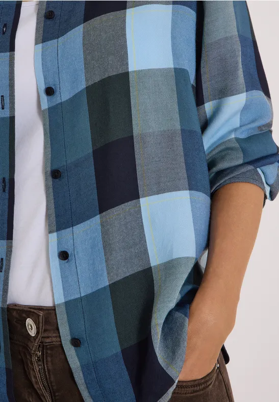 Oberkörper in blau-kariertem Hemd mit weißem T-Shirt, Hand steckt in Tasche einer braunen Hose.
