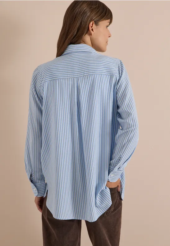 Achteraanzicht van persoon in loszittend blauw-wit gestreept overhemd met lange mouwen en bruine broek