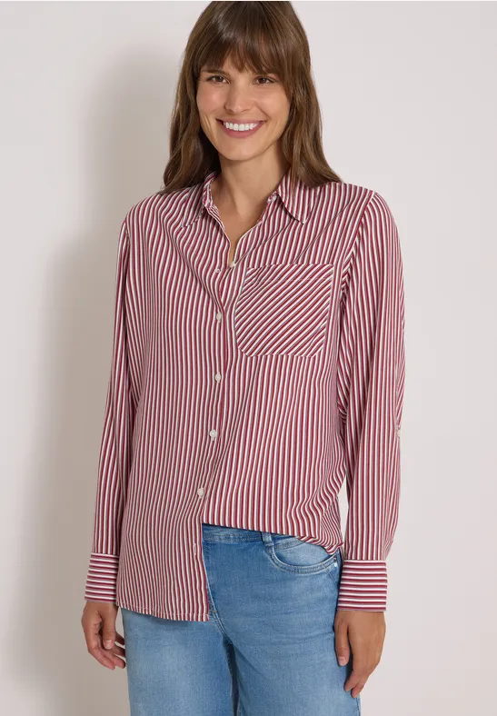 Eine lächelnde Frau trägt ein rot-weiß gestreiftes Hemd und Jeans.