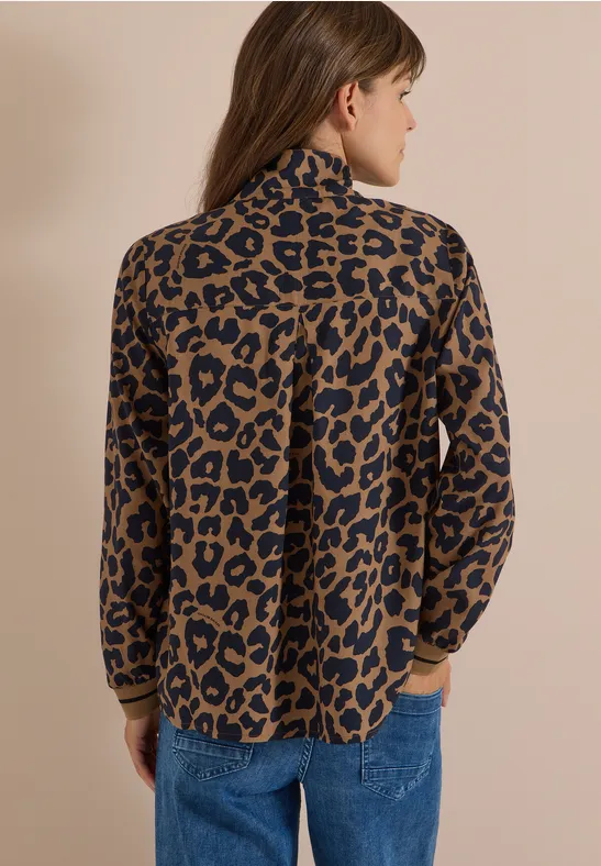 Eine Frau von hinten trägt eine lässige Bluse mit Leopardenmuster und blaue Jeans.
