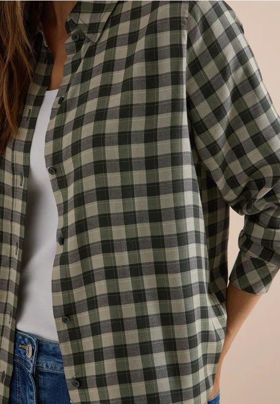 Femme en chemise à carreaux vert et beige sur débardeur blanc et jean.