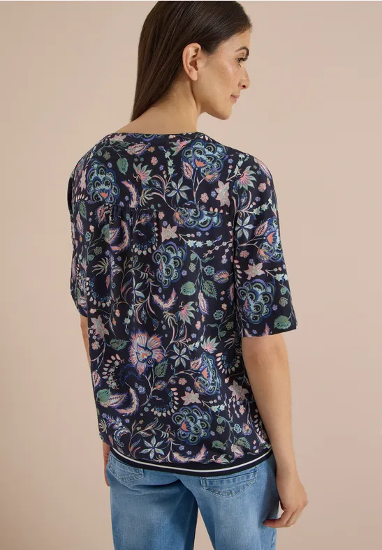 Rückansicht einer Frau in geblümter Bluse und Jeans.