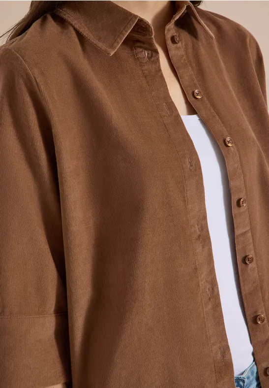 Braunes Hemd aus Leinen mit Knöpfen über weißem T-Shirt, Nahaufnahme des Oberkörpers.