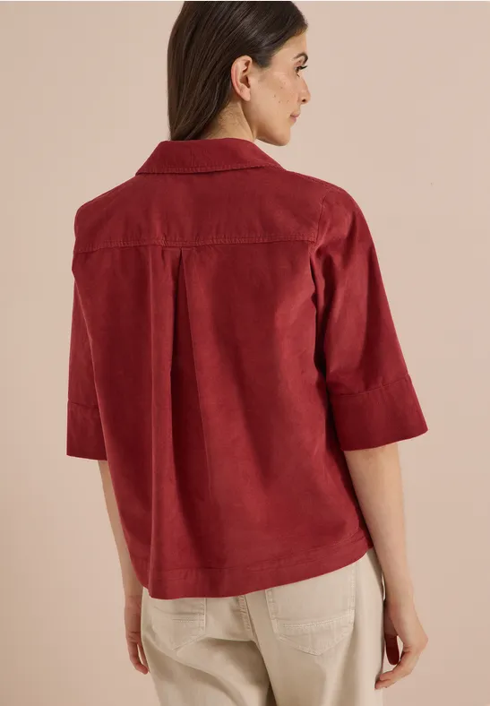 Rückenansicht einer Frau in rotem 3/4-Arm-Hemdjacke und beigen Hosen.