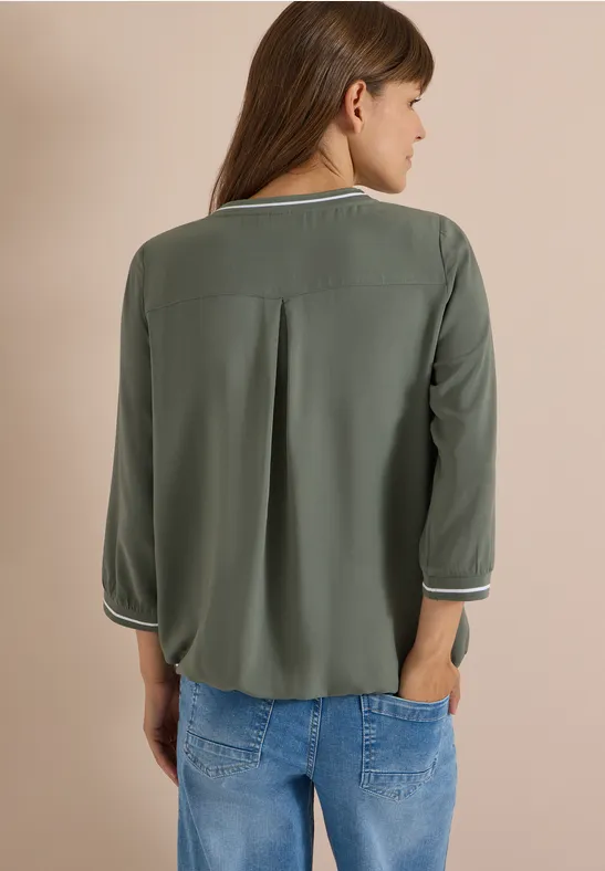 Frau von hinten in olivgrüner Bluse mit 3/4-Ärmeln und Jeans.