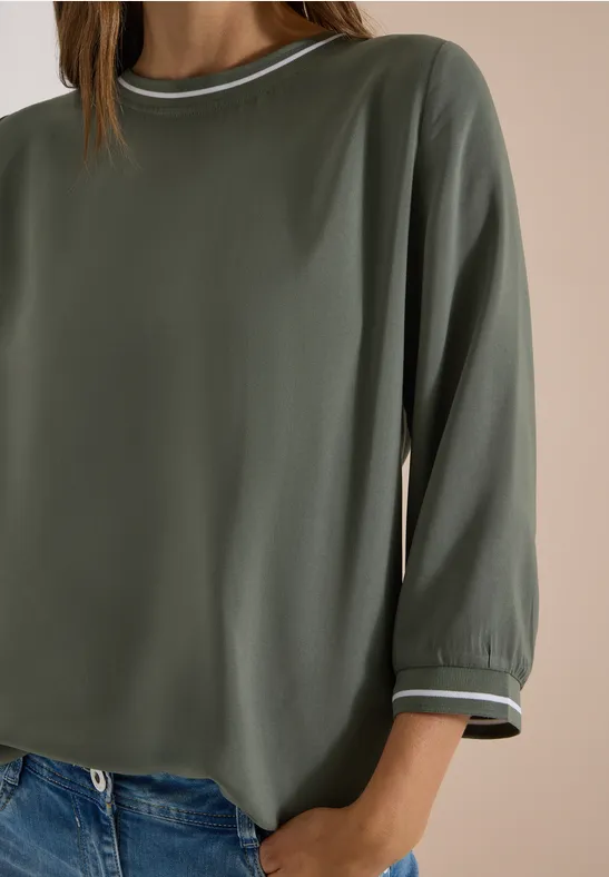 Eine lockere, olivgrüne Bluse mit 3/4-Ärmeln und weißem Paspel am Kragen und Saum.