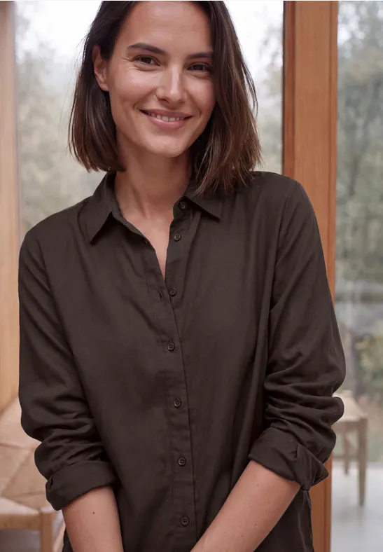 Eine lächelnde Frau in brauner Bluse vor hellem Hintergrund.