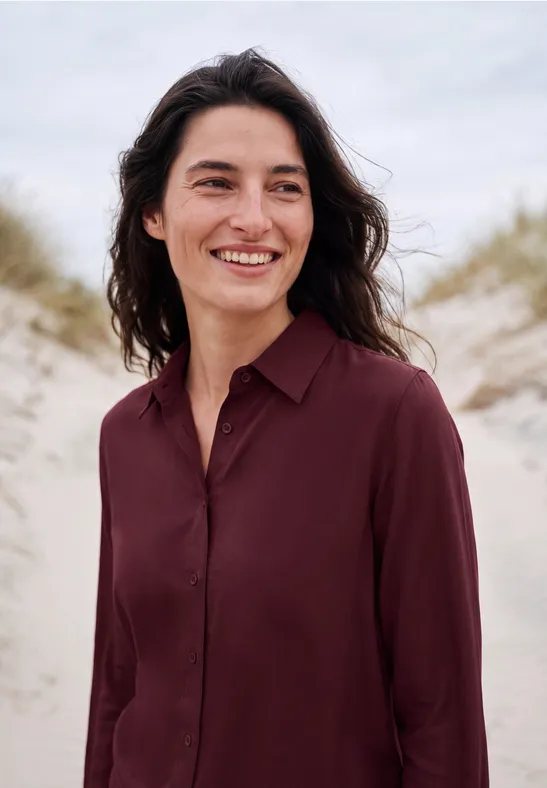 Eine Frau lächelt vor Dünen am Strand.