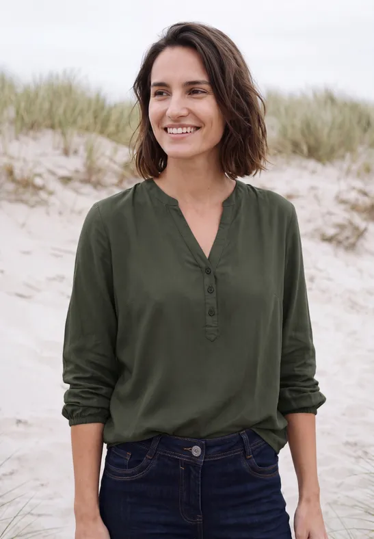 Vrouw lacht in groene blouse voor duinen aan zee