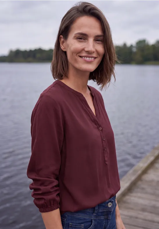 Een glimlachende vrouw staat op een steiger voor rustig water.