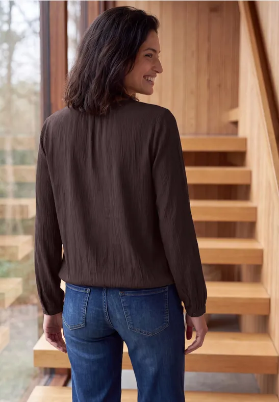 Une femme de dos jette un regard par-dessus son épaule, porte un chemisier sombre et un jean devant un escalier.