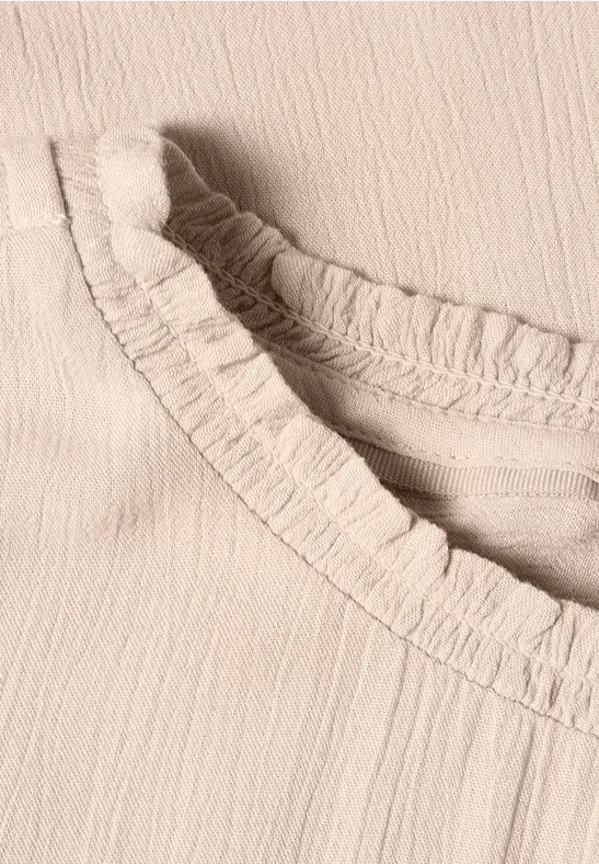 Gros plan d’un haut beige clair avec un col à volants froncés.