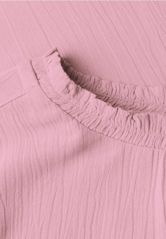 Nahaufnahme eines rosa, texturierten Stoffoberteils mit einem gerafften Kragen