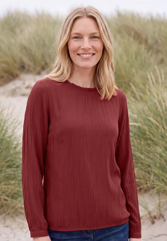 Femme souriante en haut rouge devant des herbes de dunes