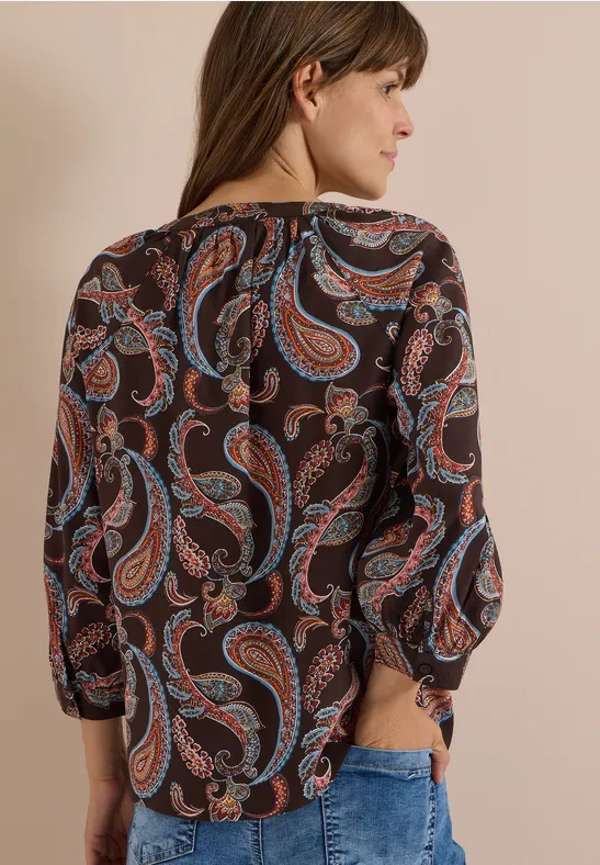 Frau von hinten in dunkelbrauner Bluse mit buntem Paisley-Muster und 3/4-Ärmeln.