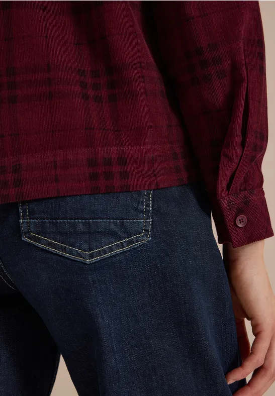 Person von hinten in roter karierter Bluse und dunkelblauen Jeans, Hand an der Seite.