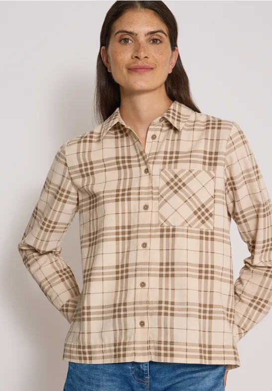 Frau trägt beige kariertes Hemd mit Brusttaschen und Jeans vor hellem Hintergrund.