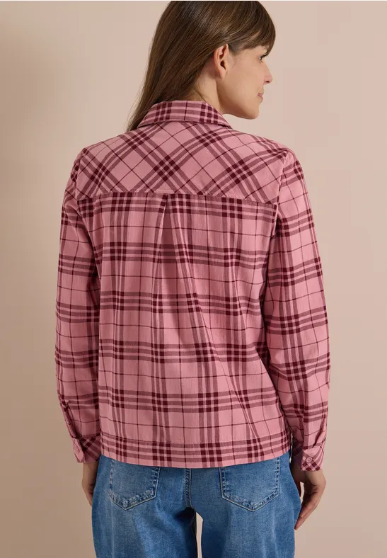 Rückansicht einer Person in rosa-kariertem Hemd und Jeans vor beigem Hintergrund.
