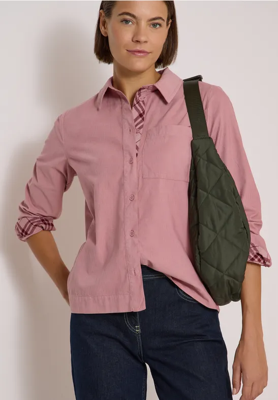 Frau in rosa Bluse und blauen Jeans trägt eine gesteppte grüne Schultertasche.