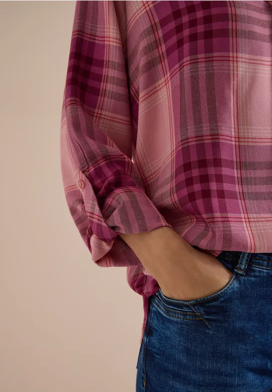 Eine Person trägt eine rosa-karierte Bluse mit hochgekrempelten Ärmeln und Jeans.