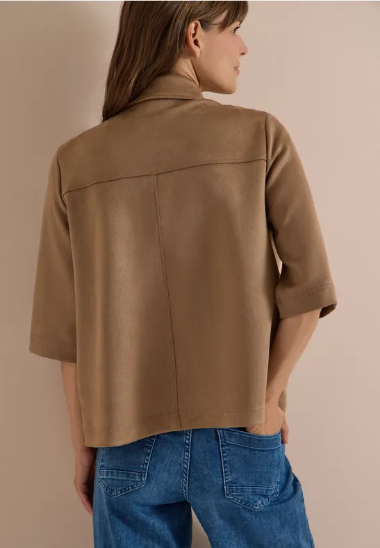 Rückenansicht einer Frau in beige-brauner, kastiger Jacke mit Dreiviertelärmeln und Jeans.