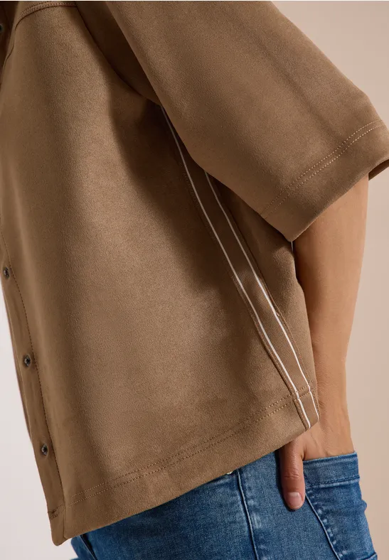 Braunes Oberteil mit Knöpfen und weißen Paspeln, Hand in der Jeans-Tasche