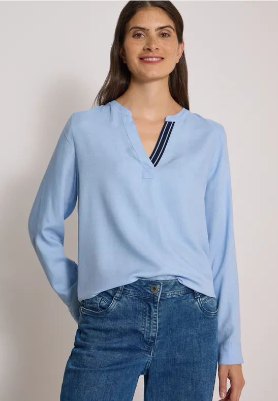 Eine Frau trägt eine hellblaue Bluse mit V-Ausschnitt und Streifendetail zu blauen Jeans.
