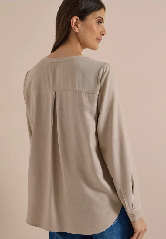 Frau trägt lockere beige Bluse mit langen Ärmeln, Rückenansicht und seitlicher Blick.