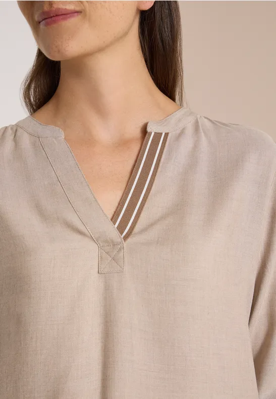 Nahaufnahme von beige Bluse mit V-Ausschnitt und drei weißen Zierstreifen am Halsausschnitt