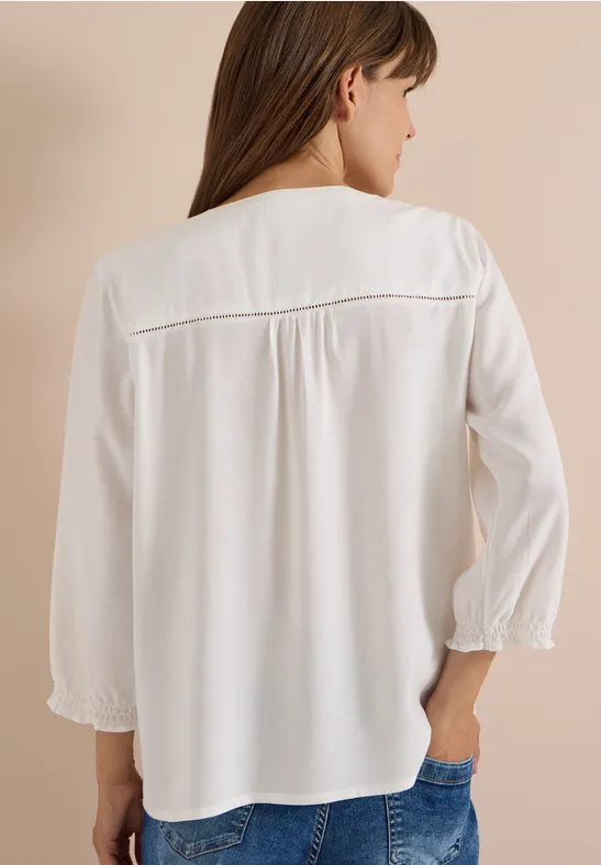Frau in weißer Bluse mit Dreiviertelärmeln, Rückenansicht, trägt Jeans.