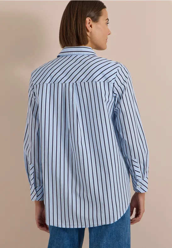 Vue de dos d’une femme portant une chemise rayée bleu et blanc avec un jean, fond neutre.