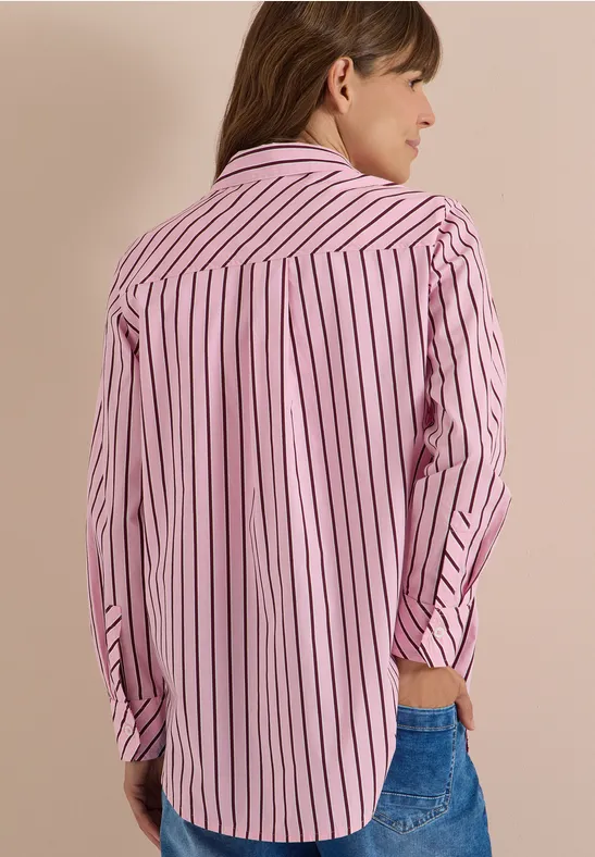Une personne vue de dos porte une chemise rose à rayures blanches et un jean.