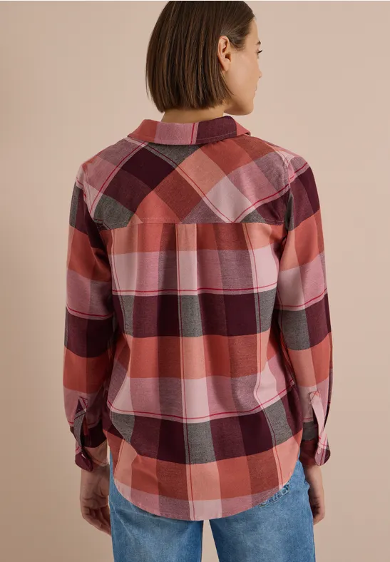 Femme vue de dos portant une chemise à carreaux rose et rouge et un jean.