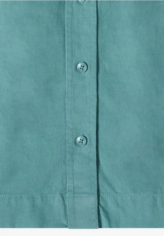 Gros plan sur une chemise turquoise à patte de boutonnage, trois boutons visibles et couture d'ourlet.